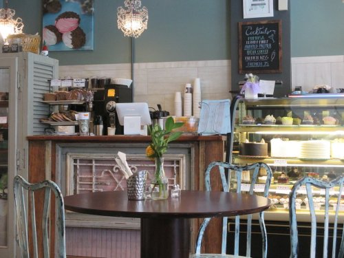 Cozy café interior with a wooden table, floral centerpiece, and a display case filled with desserts.