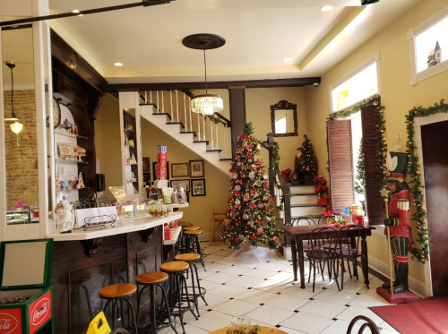 Cozy café interior decorated for Christmas, featuring a tree, festive decor, and a staircase in the background.