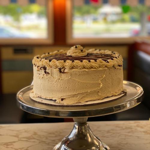 A beautifully decorated cake with creamy frosting, displayed on a silver cake stand in a bright setting.