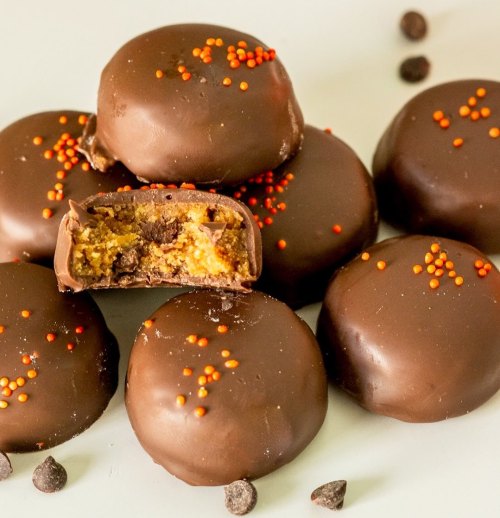 A stack of chocolate-covered treats with orange sprinkles, one cut in half to reveal a creamy filling inside.