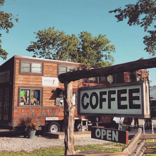 A rustic coffee shop with a wooden exterior and an "OPEN" sign hanging outside. Trees are visible in the background.