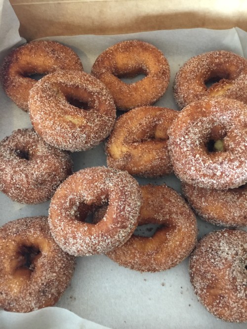 A box of freshly made, cinnamon-sugar coated donuts arranged on parchment paper.