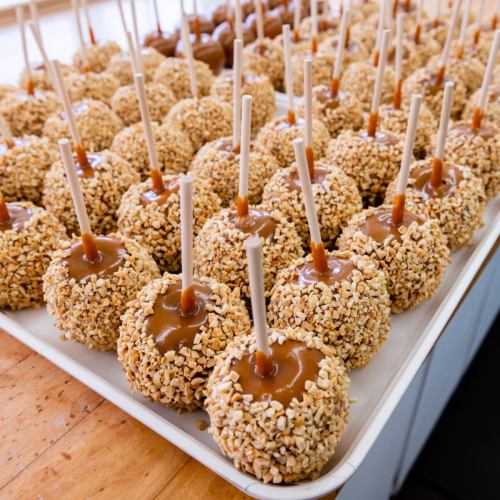 A tray of caramel apples coated in crushed nuts, each with a wooden stick for easy handling.