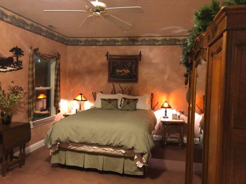 Cozy bedroom with a green bedspread, wooden furniture, and warm lighting, featuring rustic decor and a ceiling fan.