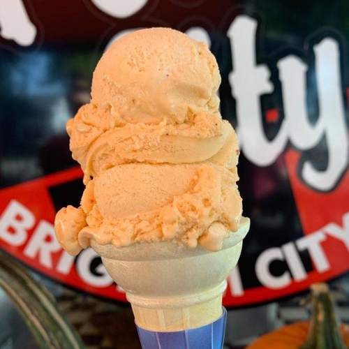 A close-up of a cone with two scoops of orange ice cream against a colorful background.