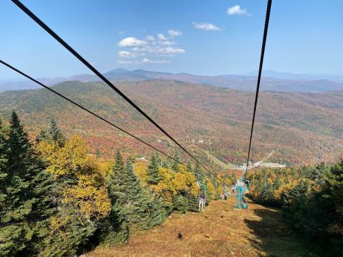 A scenic view from a ski lift, showcasing vibrant autumn foliage and mountains under a clear blue sky.