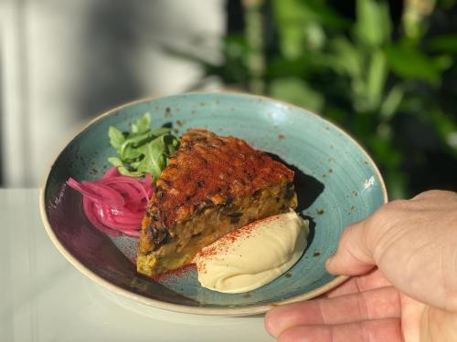 A slice of savory pie on a plate, garnished with pickled onions, greens, and a dollop of creamy sauce.