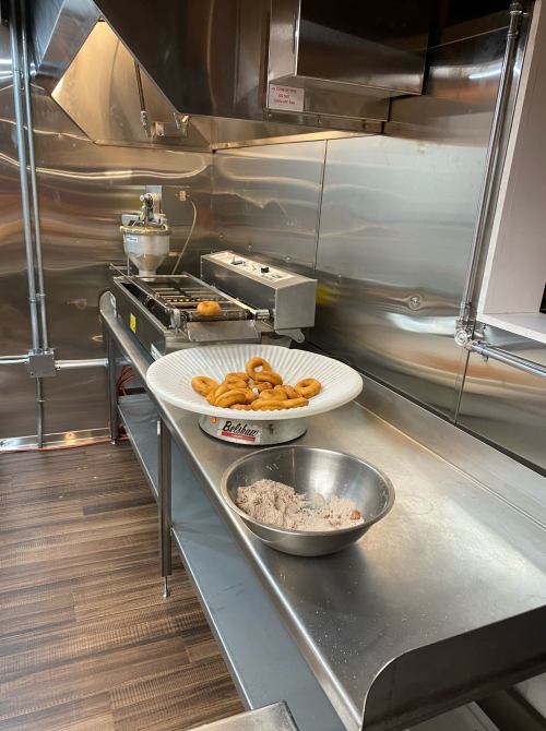 A commercial kitchen with a bowl of doughnuts and a mixing bowl on a stainless steel counter.