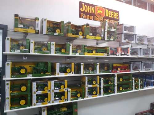 A display of various John Deere toy tractors on shelves, featuring models in green and yellow packaging.