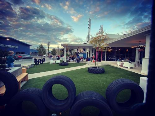 Outdoor gathering space with people seated, surrounded by tires and greenery, under a cloudy sky at dusk.