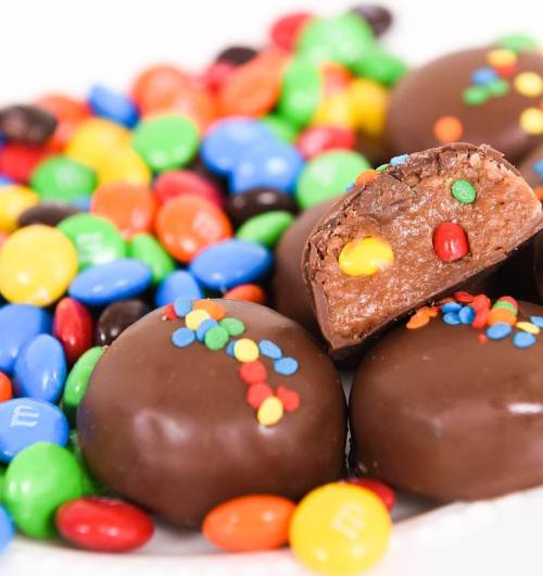 A close-up of chocolate candies with colorful candy-coated chocolates scattered around, one candy cut in half.