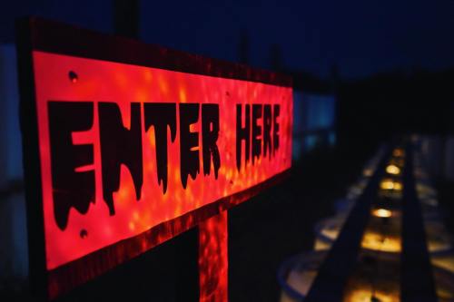 A glowing red sign reading "ENTER HERE" at night, with dimly lit pathways in the background.