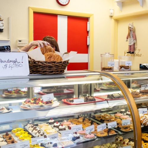 A bakery display filled with various pastries and desserts, with a person behind the counter serving a customer.