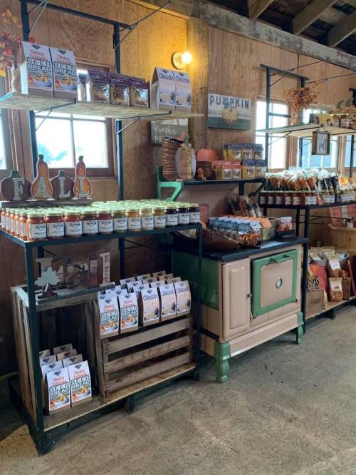A rustic market display featuring jars, snacks, and seasonal decor, with wooden shelves and a vintage stove.