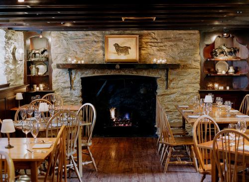 Cozy restaurant interior with wooden tables, chairs, and a stone fireplace, softly lit by candles and wall sconces.