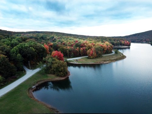 Aerial view of a serene lake surrounded by colorful autumn trees and a winding road along the shore.