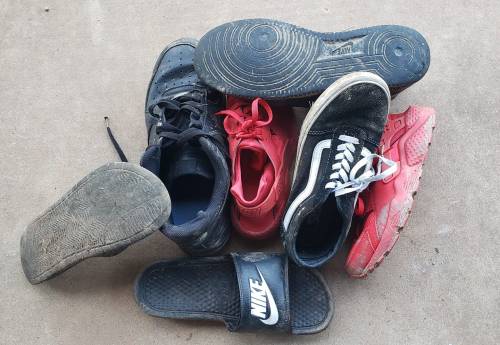 A pile of various worn shoes, including sneakers and sandals, on a concrete surface.
