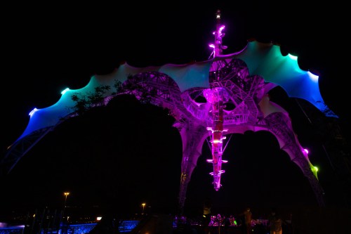 A colorful, illuminated structure with a unique design, glowing in purple and blue against a night sky.