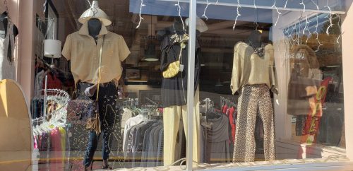 A storefront display featuring mannequins in stylish outfits, including tops and patterned pants, with decorative lights.