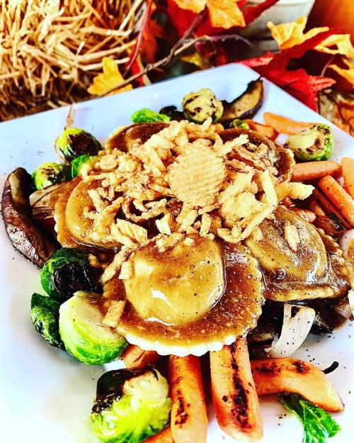 A colorful plate of ravioli topped with crispy onions, surrounded by roasted Brussels sprouts and carrots.