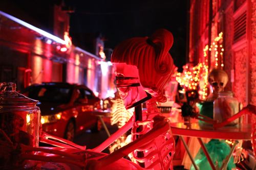 A brightly lit alley decorated for Halloween, featuring skeletons and colorful lights.
