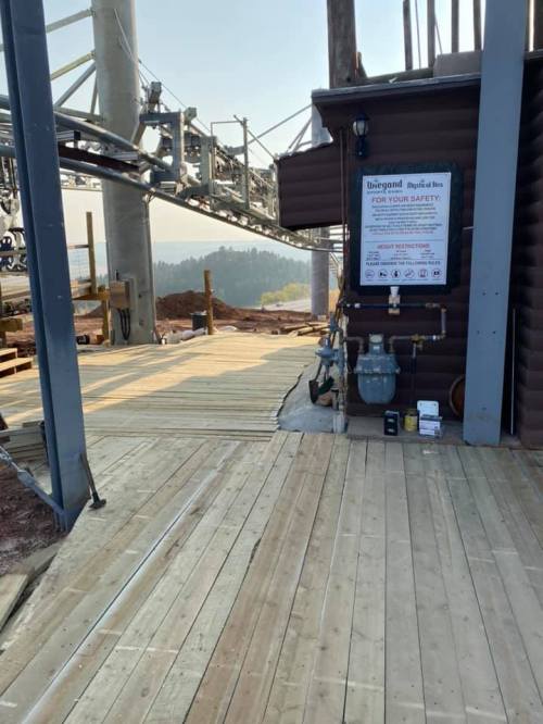 A wooden platform at a construction site with safety signage and equipment visible in the background.