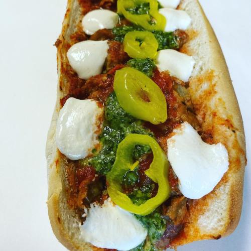 A loaded sandwich with marinara sauce, mozzarella, green peppers, and pesto on a toasted hoagie roll.