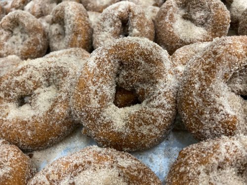 A close-up of freshly made donuts coated in sugar, arranged closely together on a surface.