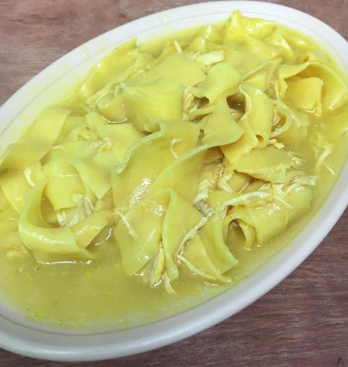 A dish of yellow noodles and shredded chicken in a savory broth, served in a white oval platter.