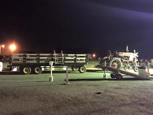 A tractor and trailer parked at night, illuminated by nearby lights, on a gravel surface.