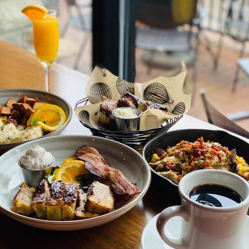 A table setting with a variety of breakfast dishes, including French toast, bacon, potatoes, and a coffee cup.