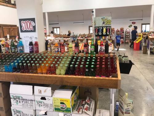 A colorful display of various soda bottles in a store, with shoppers browsing in the background.