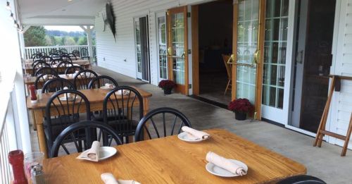 Outdoor dining area with wooden tables and chairs, featuring neatly arranged napkins and potted flowers.