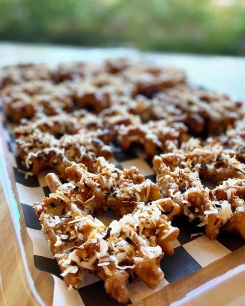 A tray of golden-brown waffles topped with shredded coconut and a drizzle of syrup, arranged neatly on a striped paper.