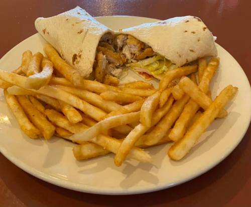 A plate with a chicken wrap partially visible and a generous serving of golden French fries.