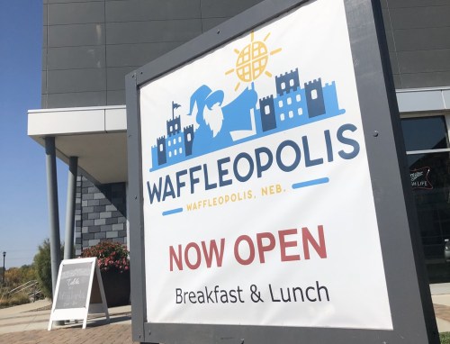 Sign for Waffleopolis, now open for breakfast and lunch, featuring a castle design and sunny graphic elements.