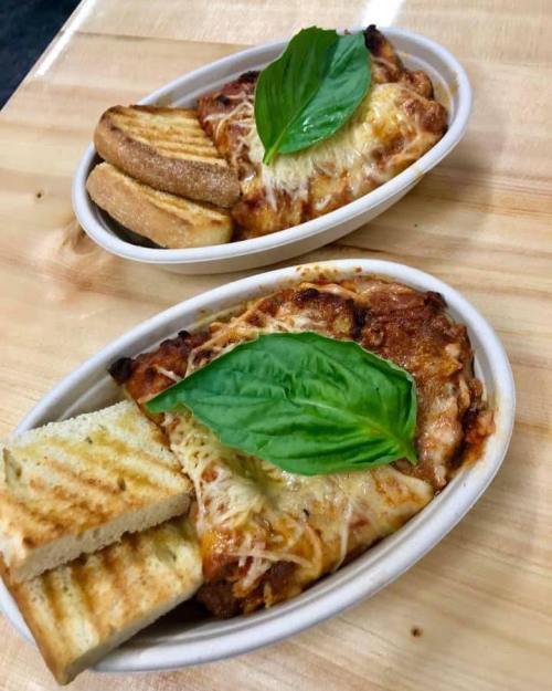 Two bowls of baked pasta topped with cheese and fresh basil, served with toasted bread on the side.