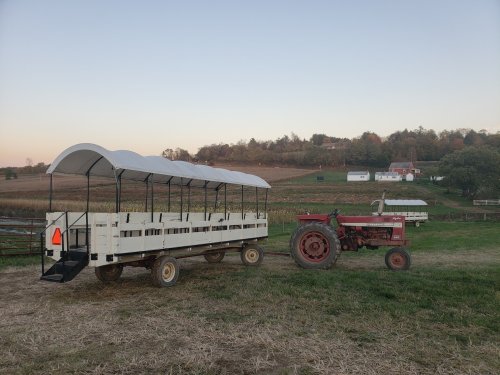 A white wagon with a canopy parked next to a red tractor in a rural farm setting at sunset.