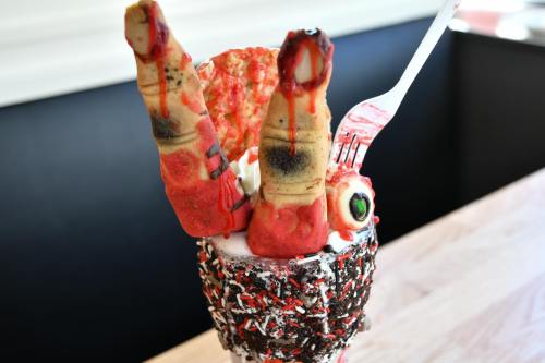 A whimsical dessert featuring a milkshake topped with cookie legs, sprinkles, and a spooky eye decoration.