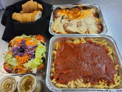 A spread of pasta with marinara, baked dish, salad, and bread rolls on a table.