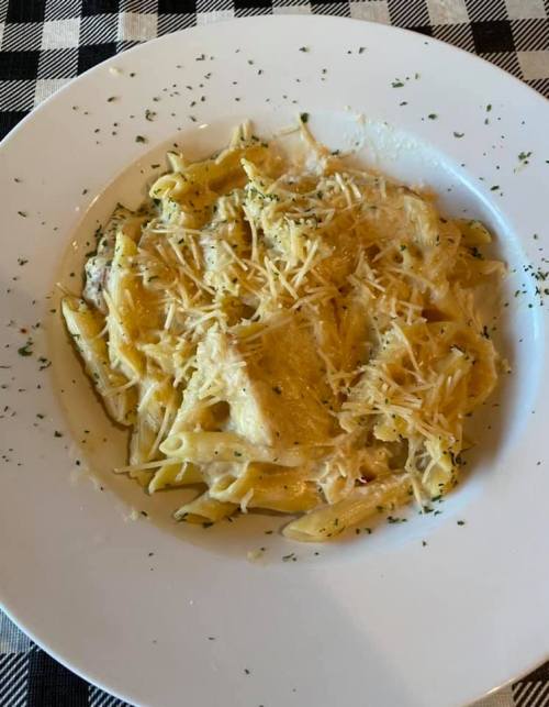 A plate of creamy pasta with penne, topped with grated cheese and sprinkled with herbs, on a checkered tablecloth.