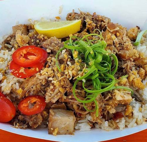A bowl of rice topped with shredded meat, sliced tomatoes, green onions, and a lemon wedge.