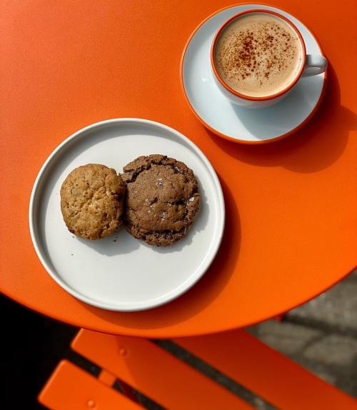 A plate with two cookies and a cup of coffee on an orange table.