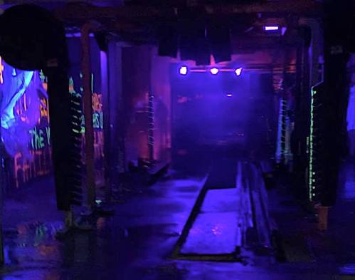Dimly lit indoor space with purple lights, featuring graffiti and wet floors, creating an eerie atmosphere.