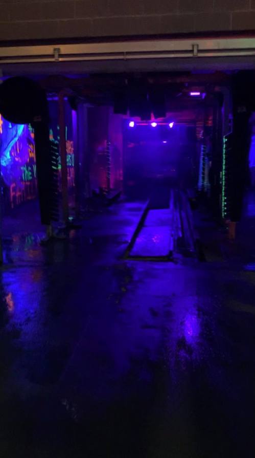A dimly lit space with purple lights reflecting on a wet floor, featuring colorful wall art in the background.
