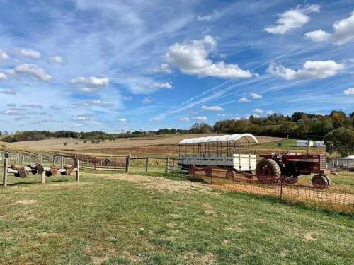 A scenic farm landscape featuring a tractor, a wagon, and rolling hills under a blue sky with fluffy clouds.