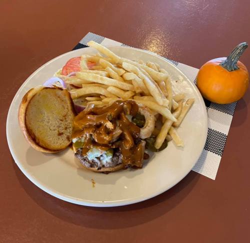 A plate with a burger topped with green peppers and gravy, served with fries and a small pumpkin on the side.