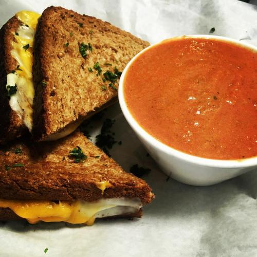 Grilled cheese sandwich with melted cheese on whole grain bread, served with a bowl of tomato soup.