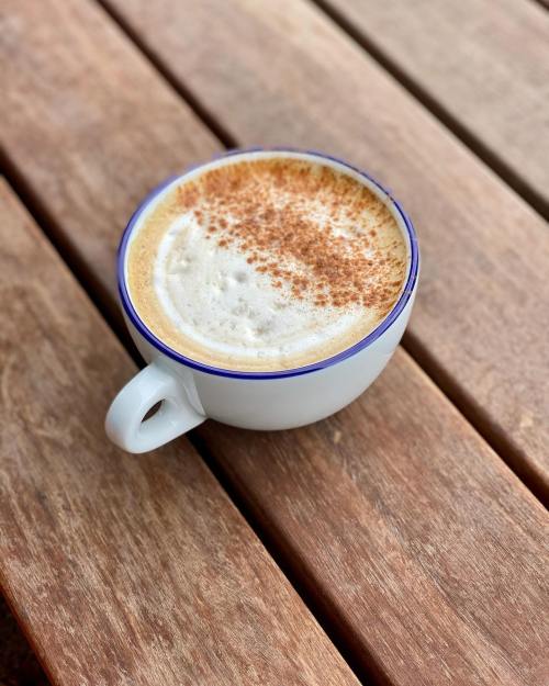 A white coffee cup with frothy coffee topped with cinnamon, resting on a wooden table.