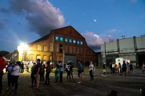 A crowd gathers outside a historic building labeled "PULLMAN" at dusk, with a bright moon in the sky.